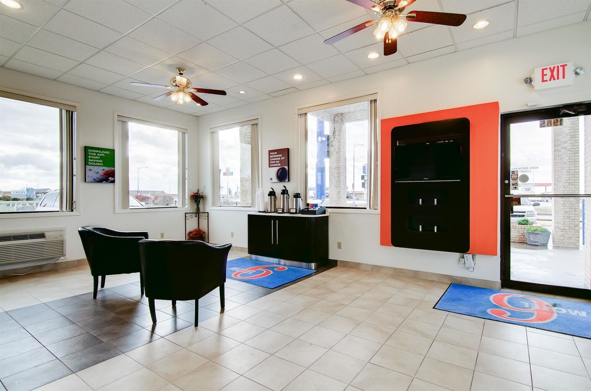 A hotel lobby with two black chairs, a black cabinet, a ceiling fan, and a red exit sign.