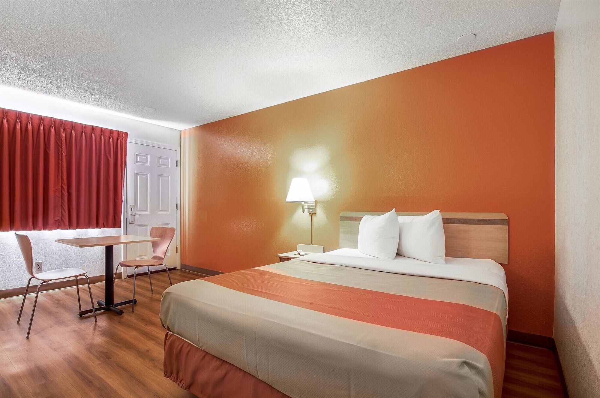 A hotel room with a bed, a desk, a chair, and a lamp.