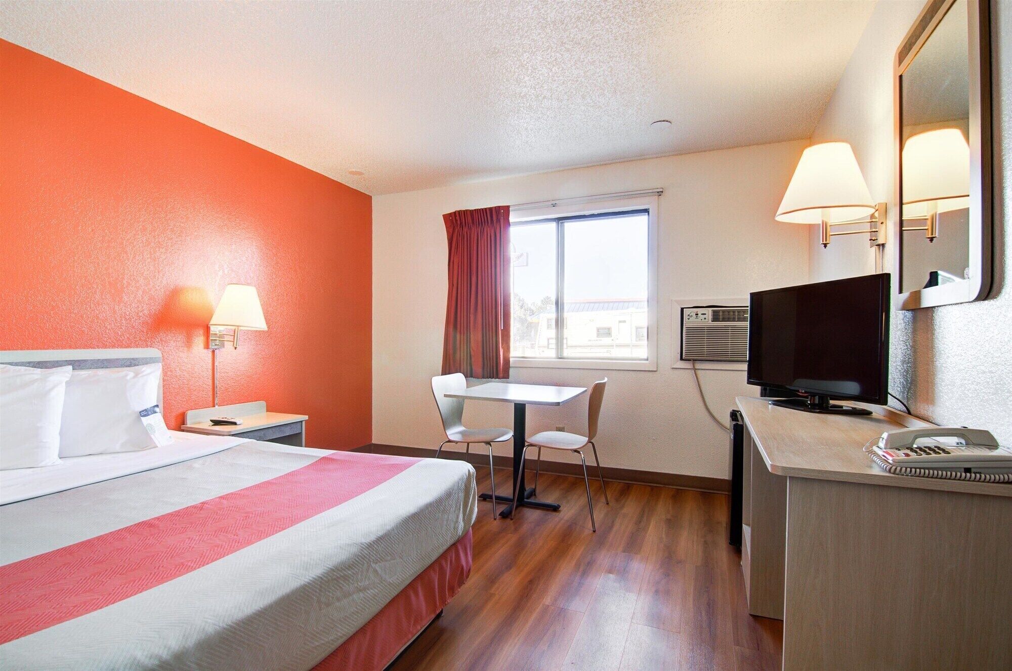 A hotel room with a bed, desk, chair, TV, and window.