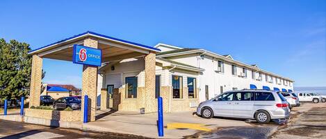 Un motel doté d’une entrée couverte, d’une enseigne indiquant qu’il y a six bureaux, et d’un parking où sont stationnées plusieurs voitures.