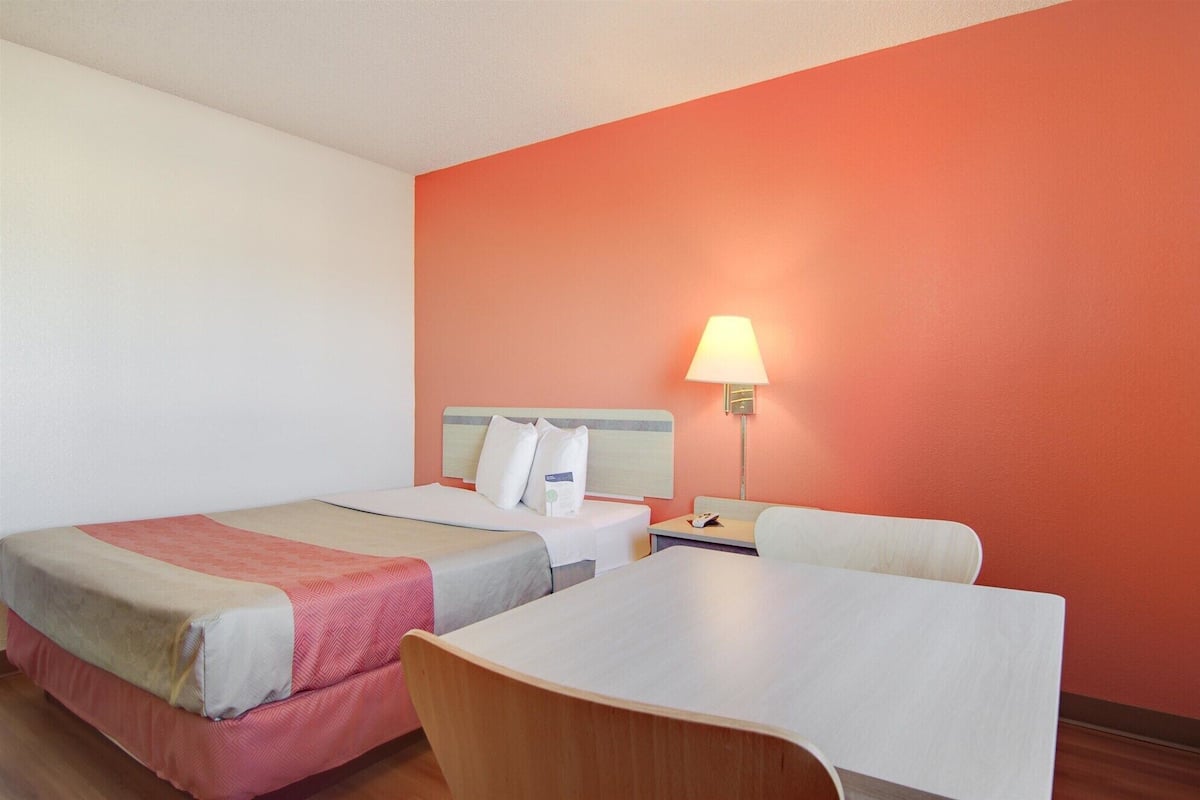A hotel room with two beds, a table, and a lamp.