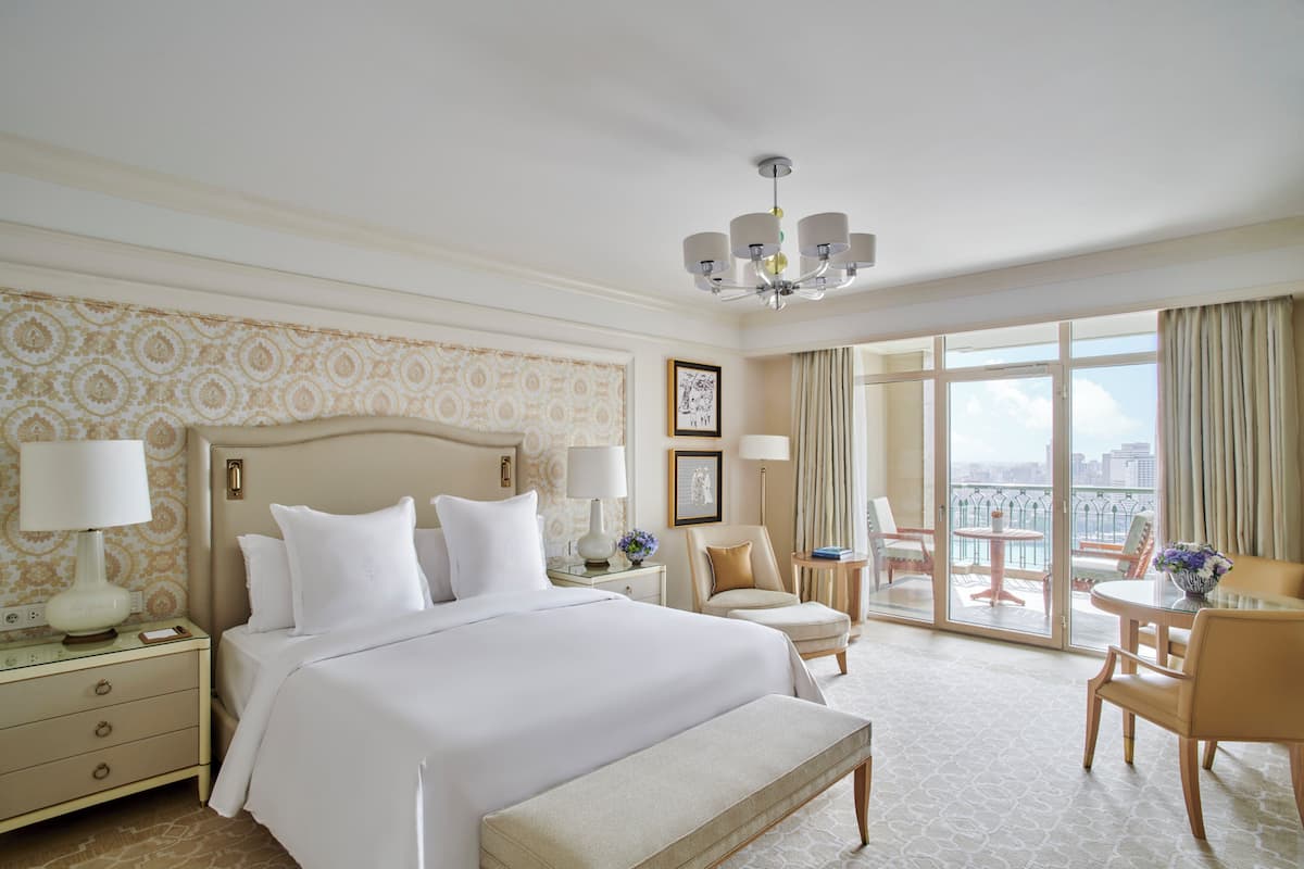 Ein Hotelzimmer mit einem großen Bett, einer Sitzecke mit Tisch und Stühlen, einem Balkon mit Aussicht und einer Kristallleuchtre.