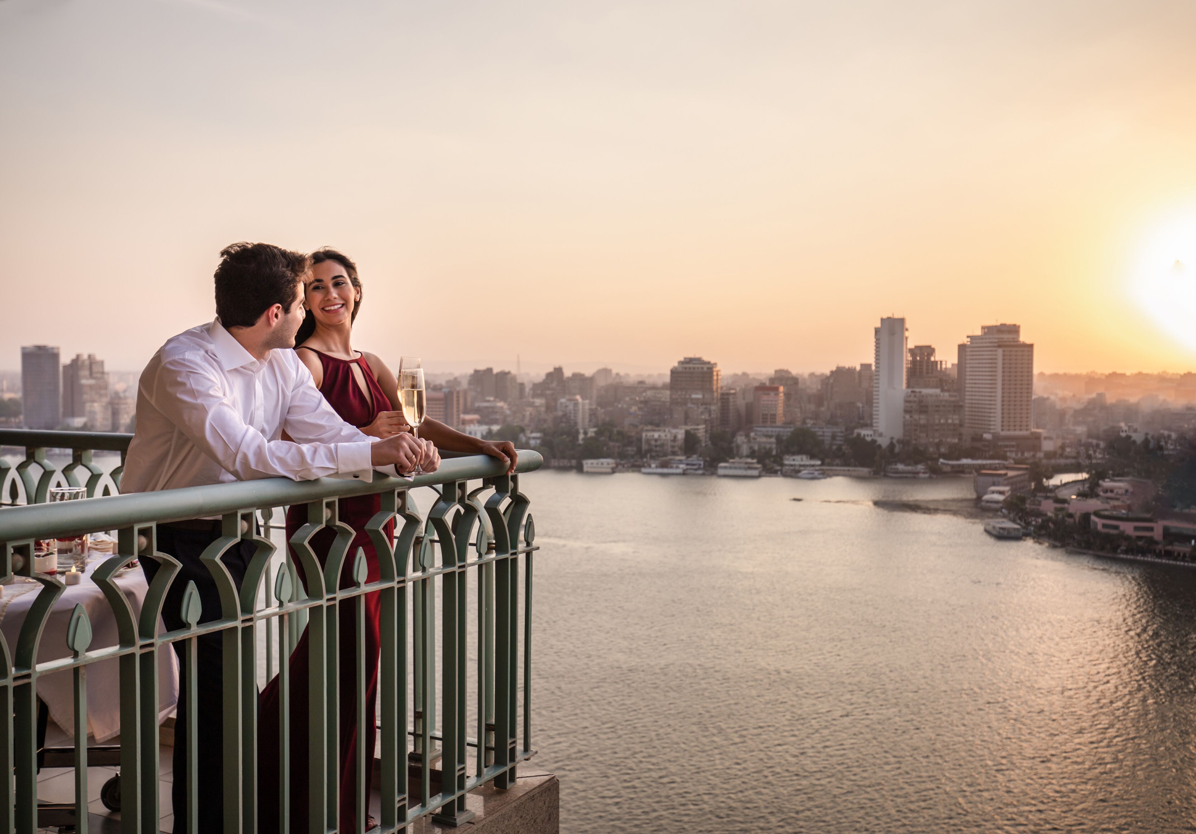 A couple overlooking a cityscape with a river at sunset.