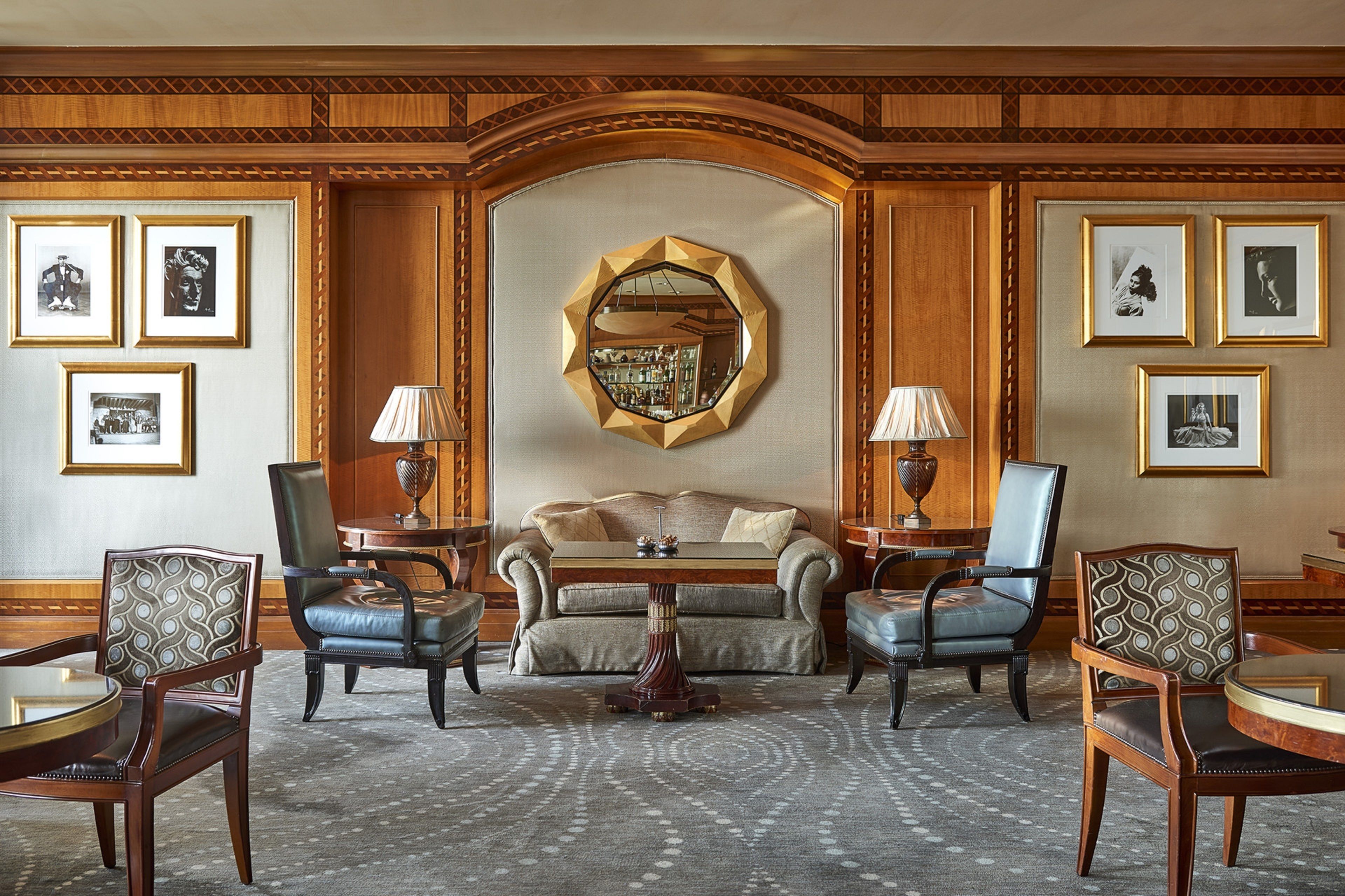 A formal sitting room with a sofa, two armchairs, a coffee table, and a round table. There are framed pictures on the walls and a large mirror above the sofa.