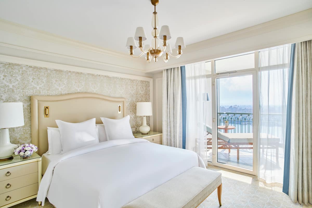 Ein geräumiges Schlafzimmer mit einem großen Bett, zwei Nachttischen mit Lampen, einer Chandelier und einem Balkon mit Blick.