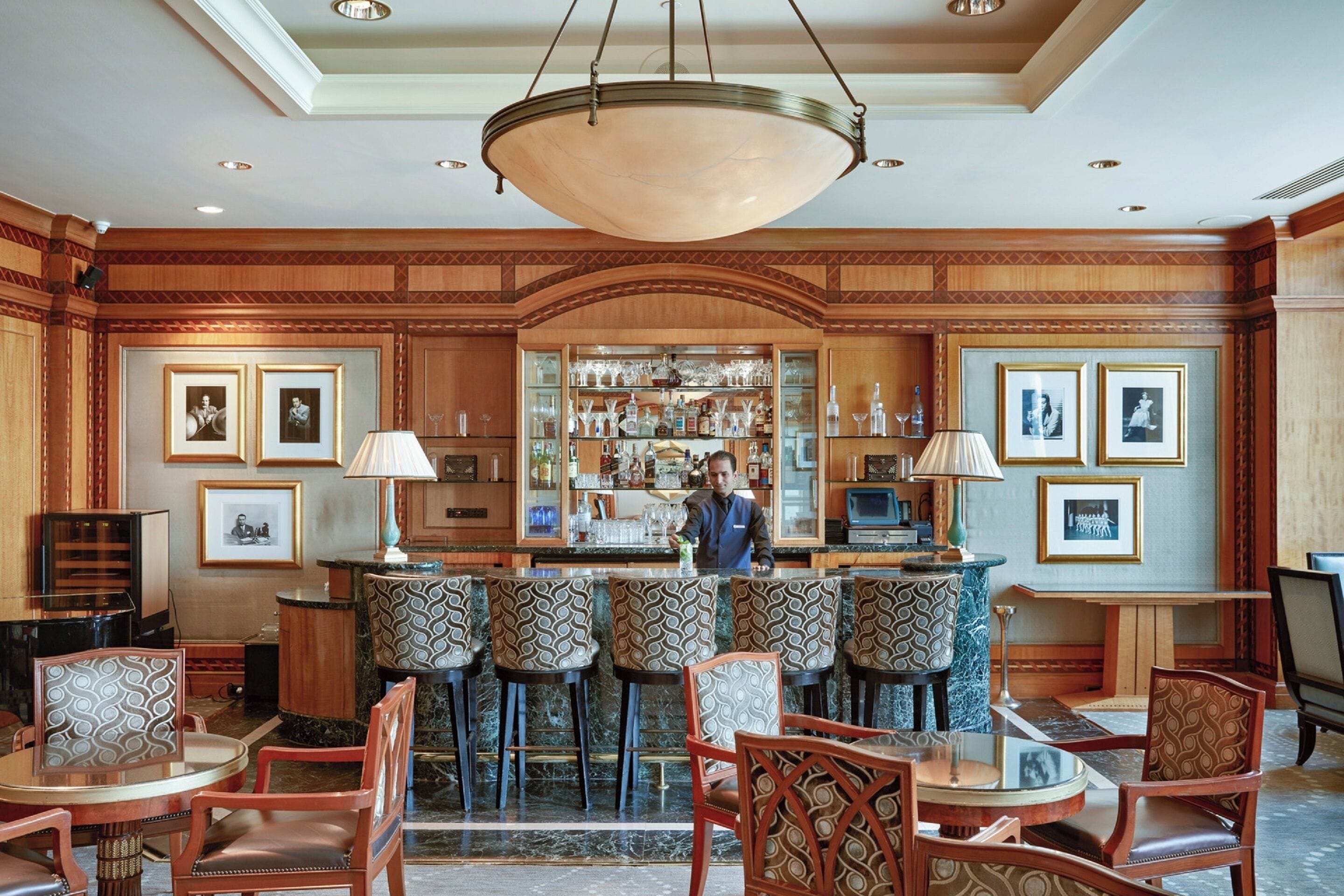 A bar area with a bartender, patterned bar stools, and framed pictures on the walls.