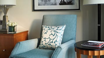 A room with a blue armchair, a matching ottoman, a small wooden side table with a book, and two framed black-and-white photographs on the wall.