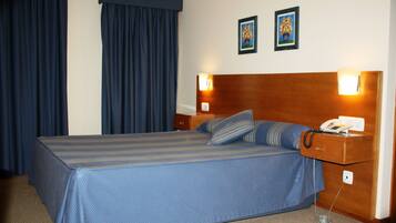 Quarto de hotel com cama, mesa de cabeceira, telefone e duas fotos emolduradas na parede.