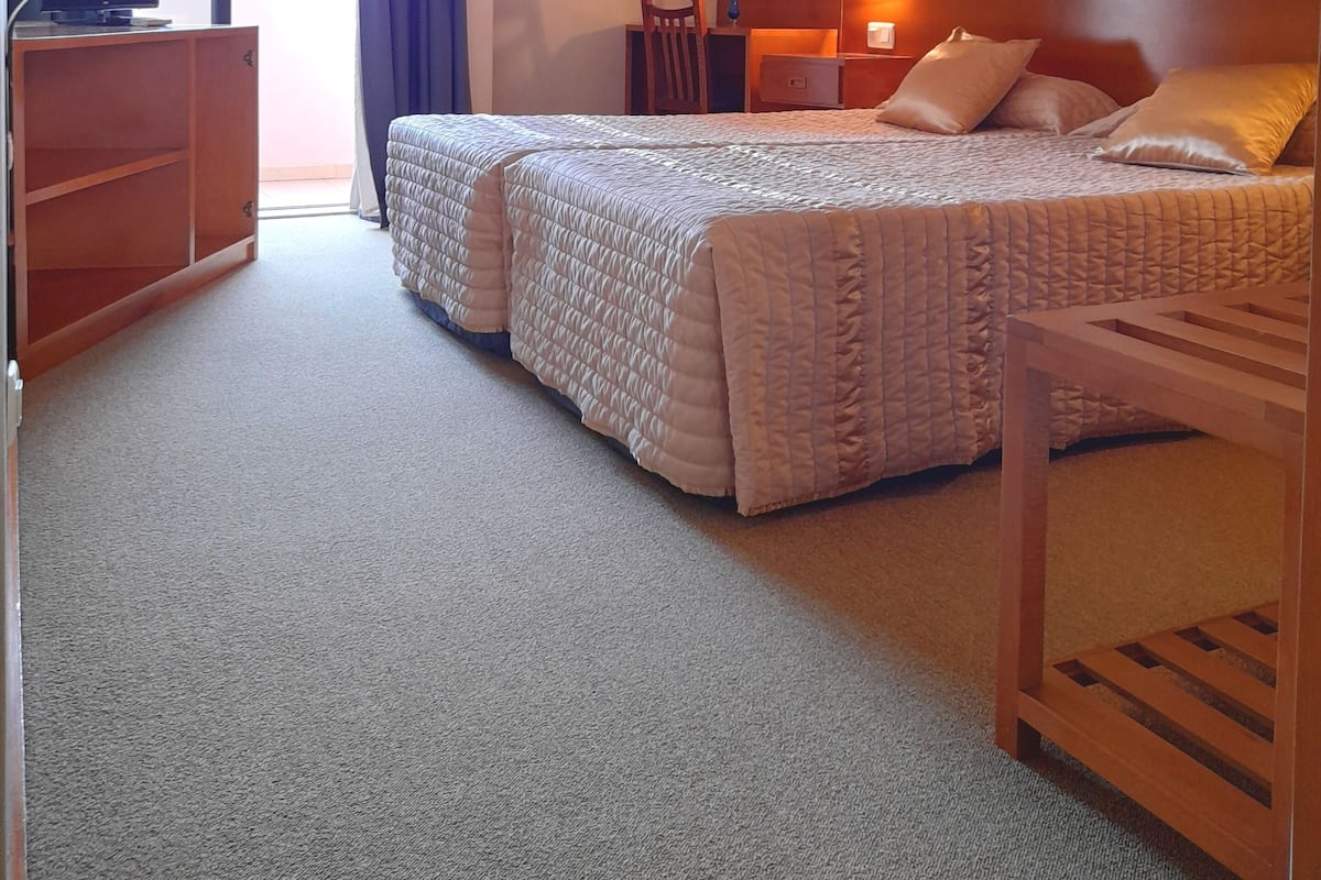 A hotel room with two beds, a desk, a chair, a TV, and an air conditioning unit.