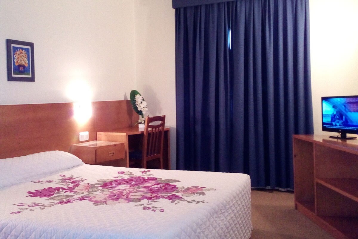 A hotel room with a bed, a desk, a chair, a television, and a window with curtains.