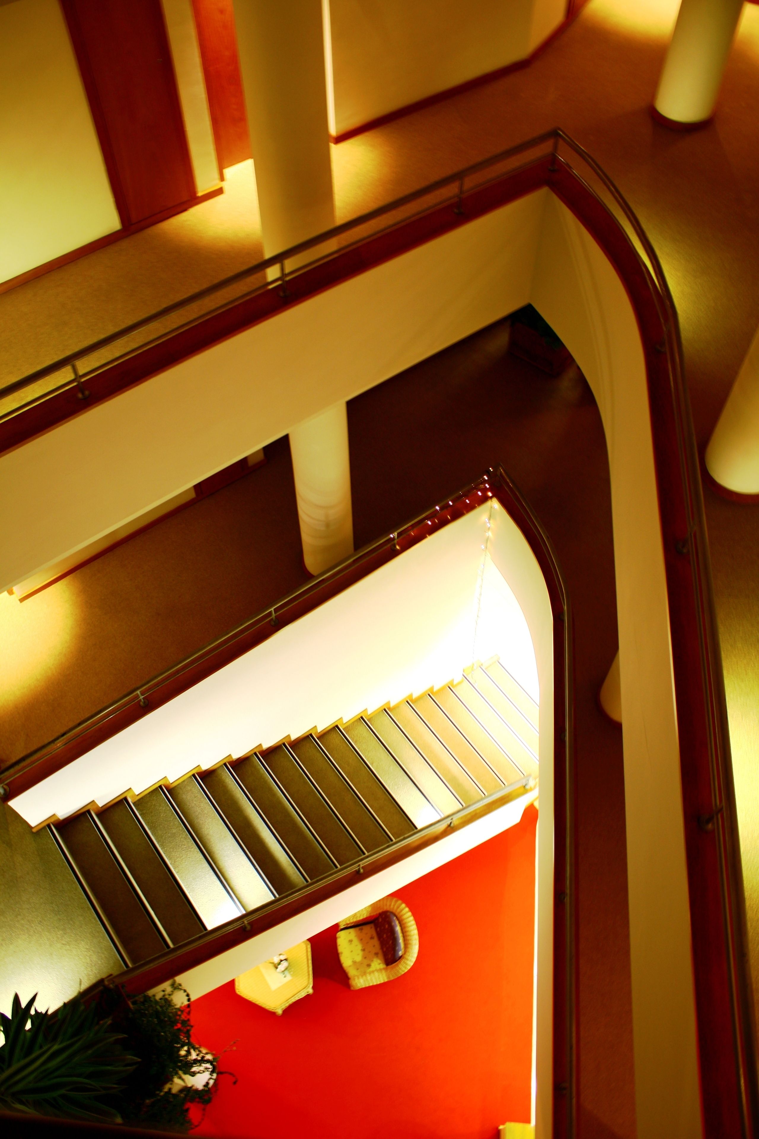 Una escalera con barandilla de vidrio y pared roja en la parte inferior.