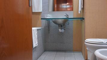 A bathroom with a glass sink, a toilet, and a mirror.
