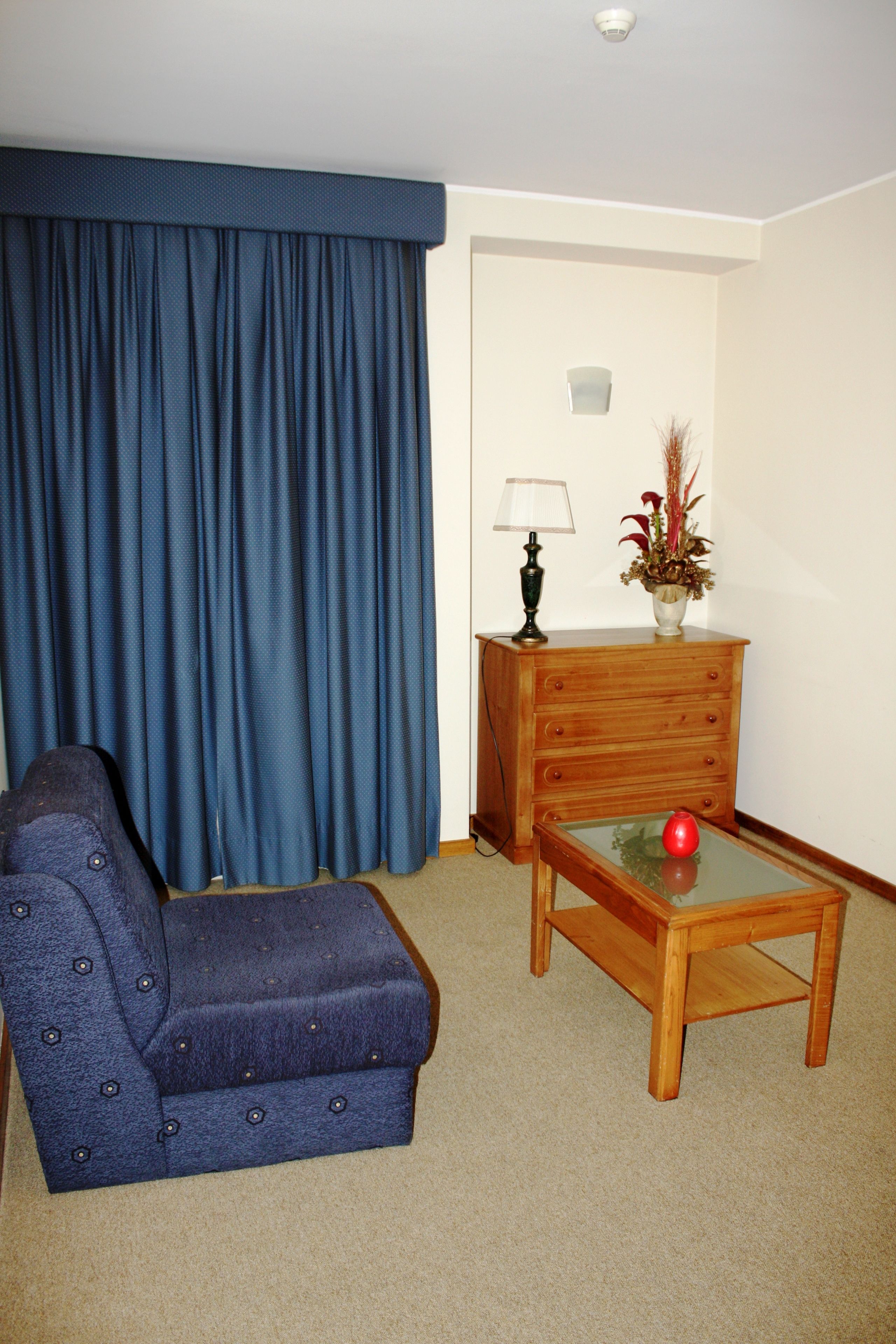 Una habitación con un sofá azul, una mesita de madera con un jarrón rojo y una lámpara.