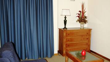 Una habitación con un sofá azul, una mesita de madera con un jarrón rojo y una lámpara.