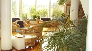 A sunlit room with wicker furniture and large windows overlooking greenery. - Hotel das Taipas (Guimarães)