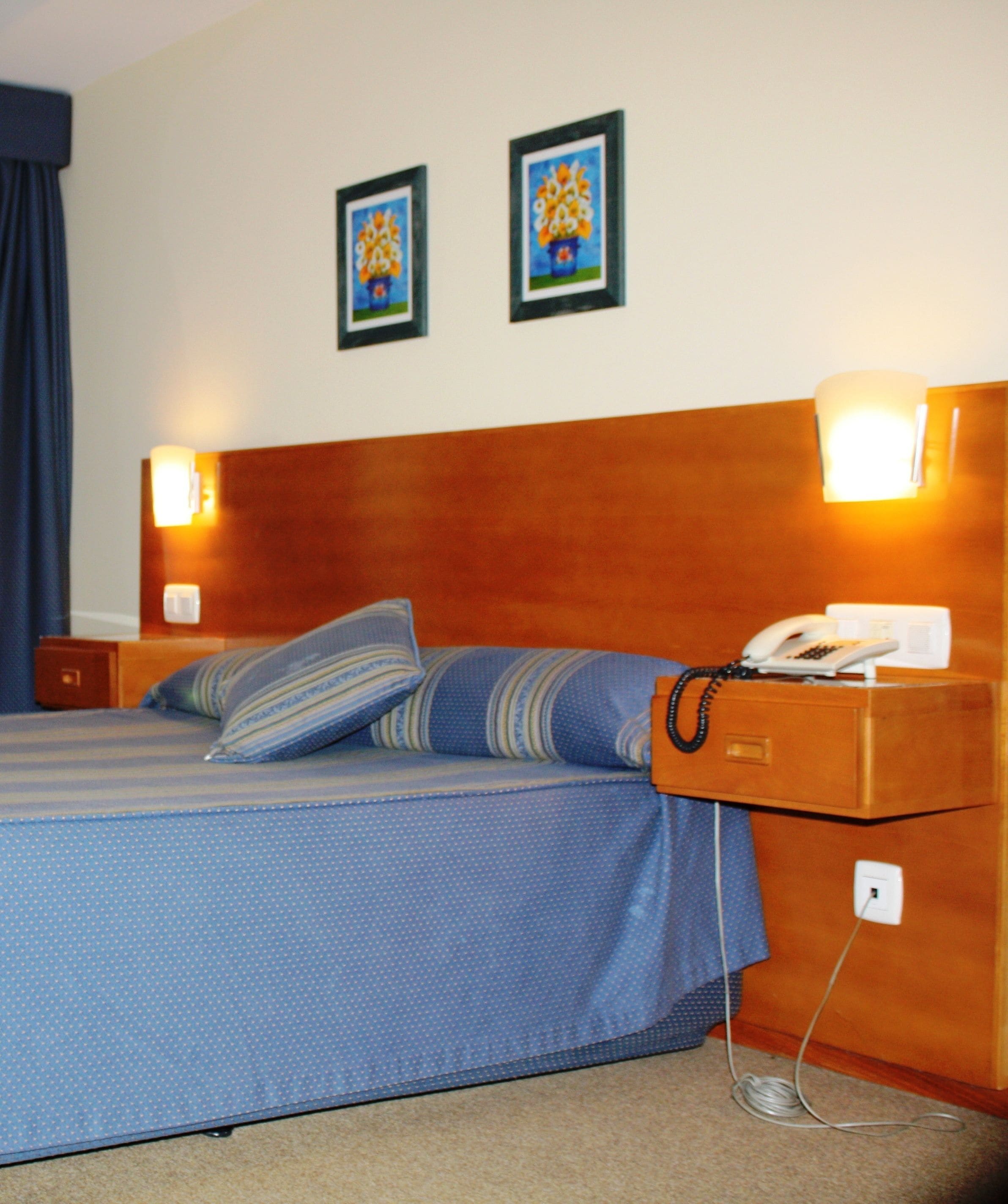 Een hotelkamer met een bed, een telefoon en twee wandlampen.