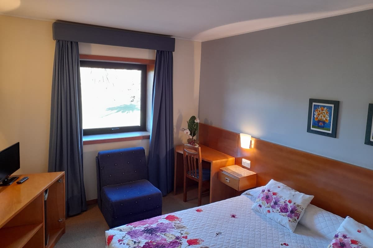 A hotel room with a bed, a desk, a chair, a TV, and a window with curtains.