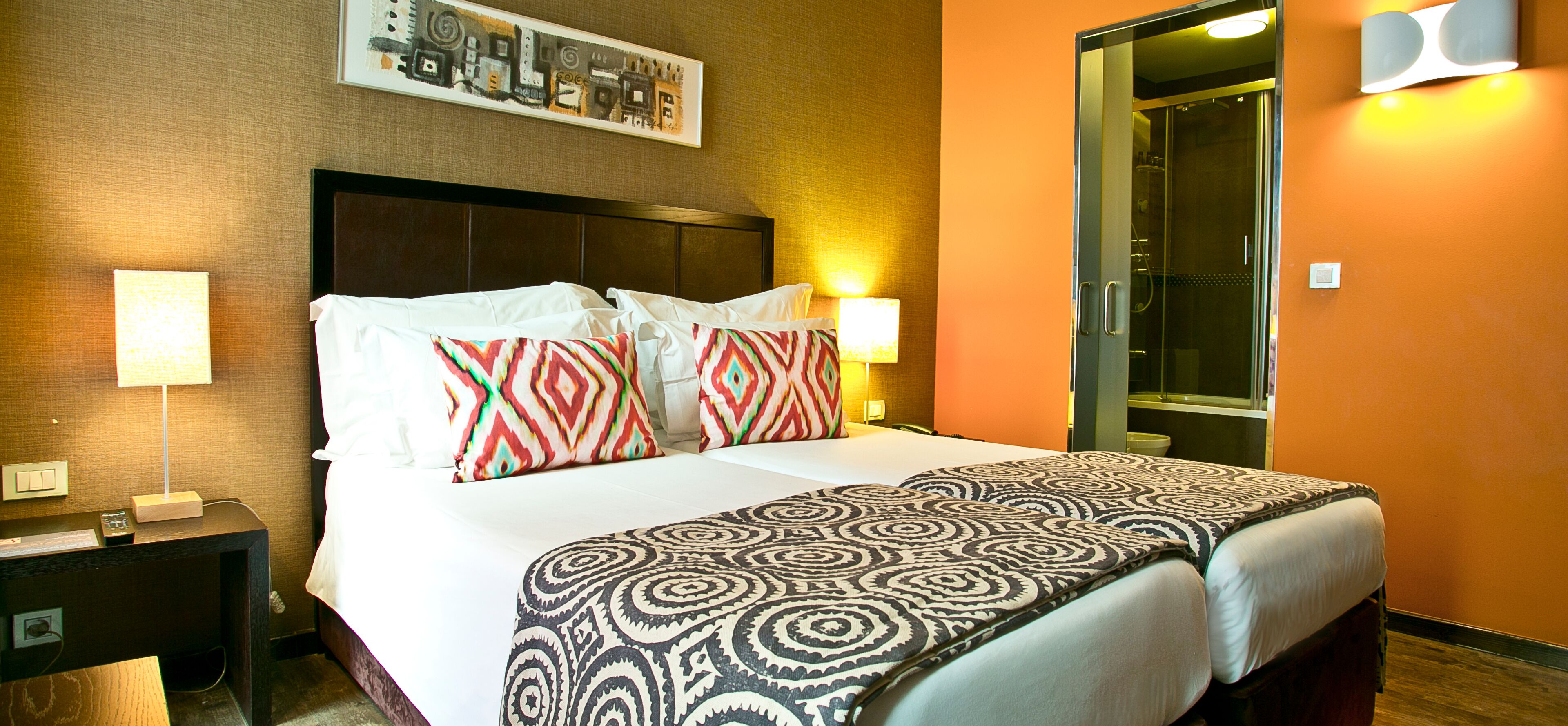 Habitación de hotel con una cama grande, dos lámparas de noche, una mesita de noche y una puerta al baño.