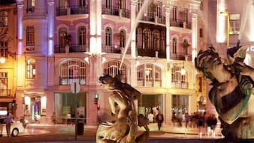 Ein Hotel mit einer klassischen Fassade, mehreren Balkonen und einem Brunnen mit Statuen.