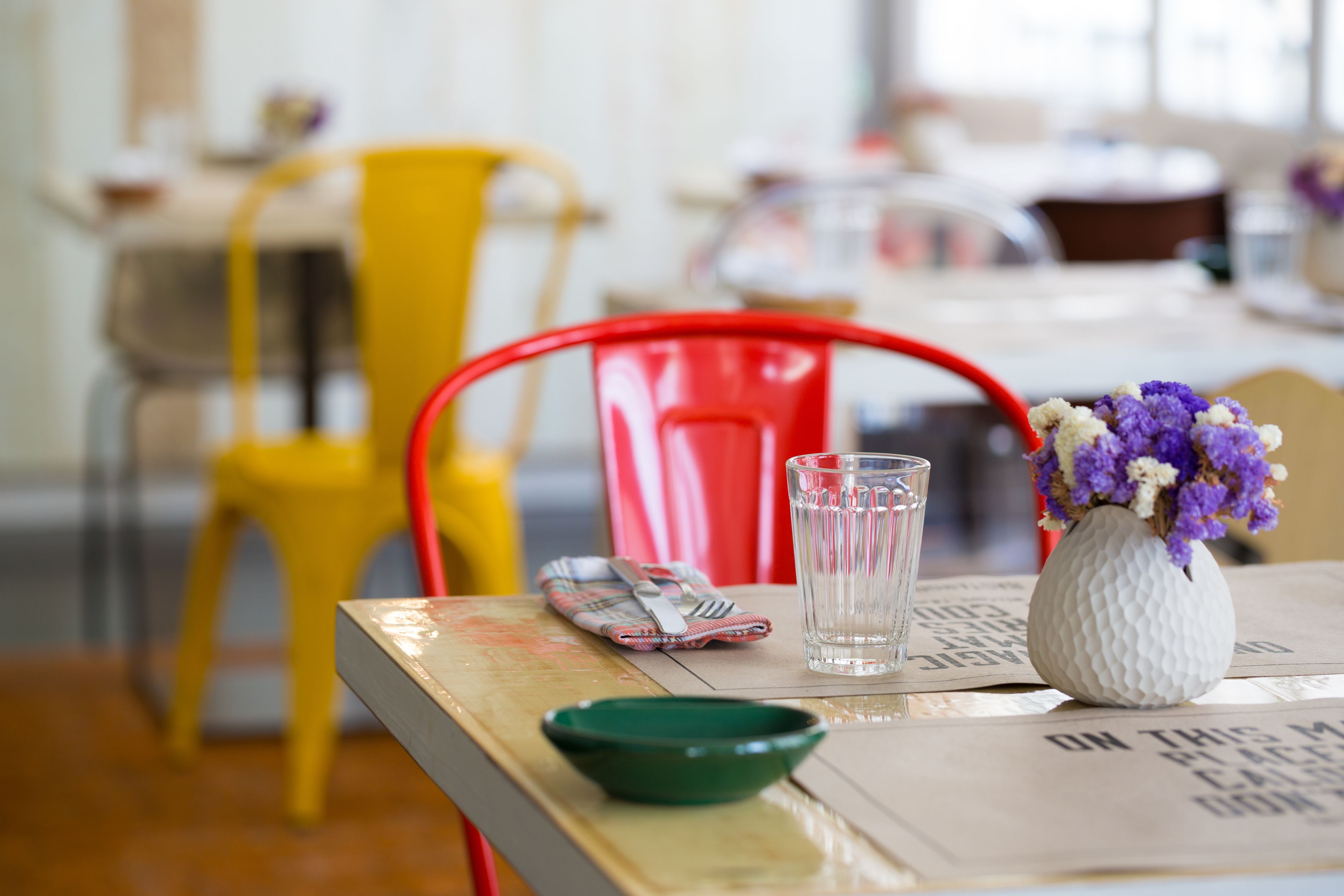A dining table with a white vase, a glass of water, a green bowl, and a napkin with utensils.