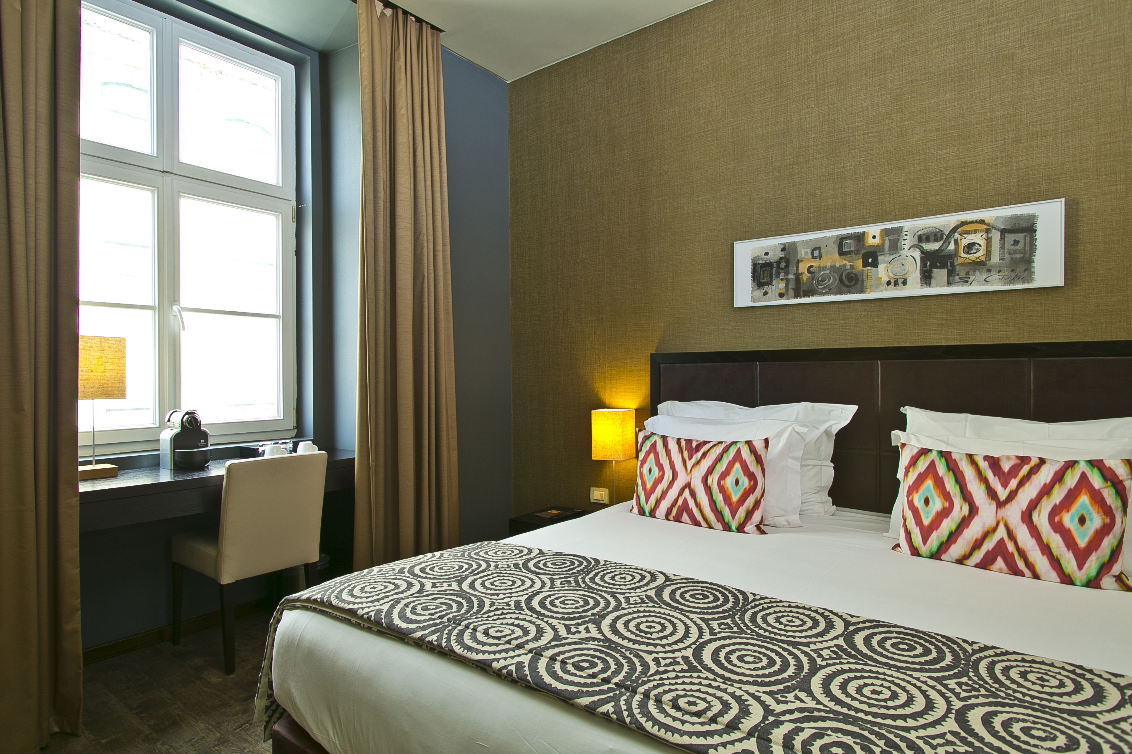 A hotel room with a large bed, a desk, and a window with curtains.