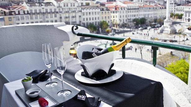 A table set with a bottle of champagne, glasses, a small dish with a strawberry, and a napkin with the text "NAOKI". - Internacional Design Hotel (Lisbon)