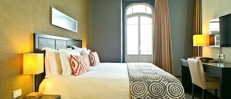 A hotel room with a large bed, a desk, a chair, a lamp, and a window with curtains.