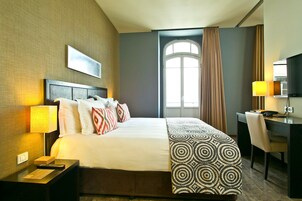 A hotel room with a large bed, a desk, a chair, a lamp, and a window with curtains.