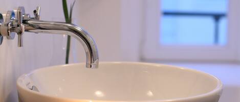 A bathroom with a white sink, two candles, and a purple flower in the background.