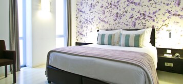 Un lit bien fait, avec une literie à rayures, un papier peint à motifs floraux et une table de chevet sur laquelle se trouvent une lampe et un téléphone.