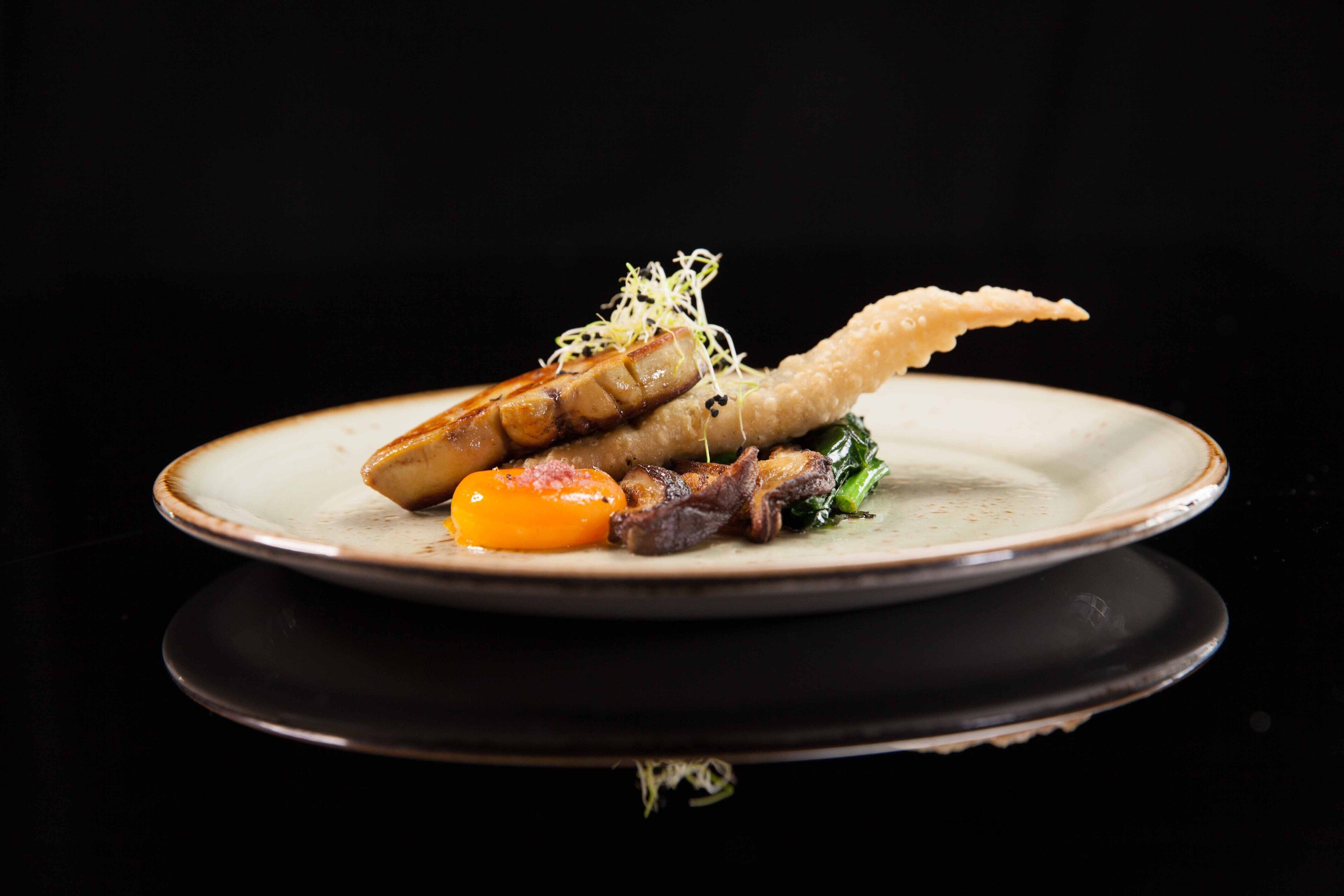 Plat amb diverses maneres de menjar, incloent carn, verdura i un plat fregit, tot disposat sobre un plat de ceràmica.