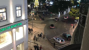 A nighttime view of a city square with a large Christmas tree, people walking, and cars parked.