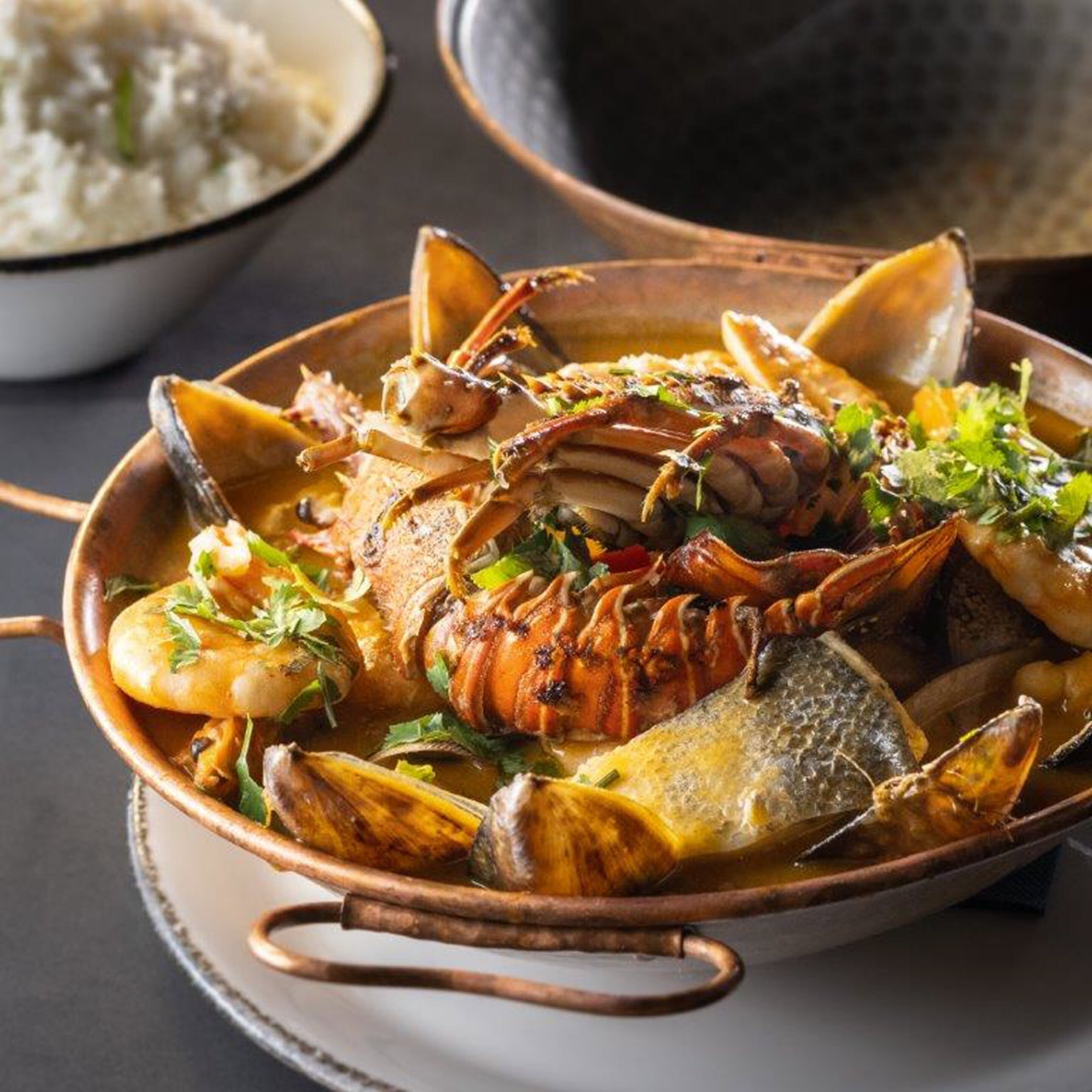 Un plato de mariscos en un bol de cobre con asa, adornado con hierbas.