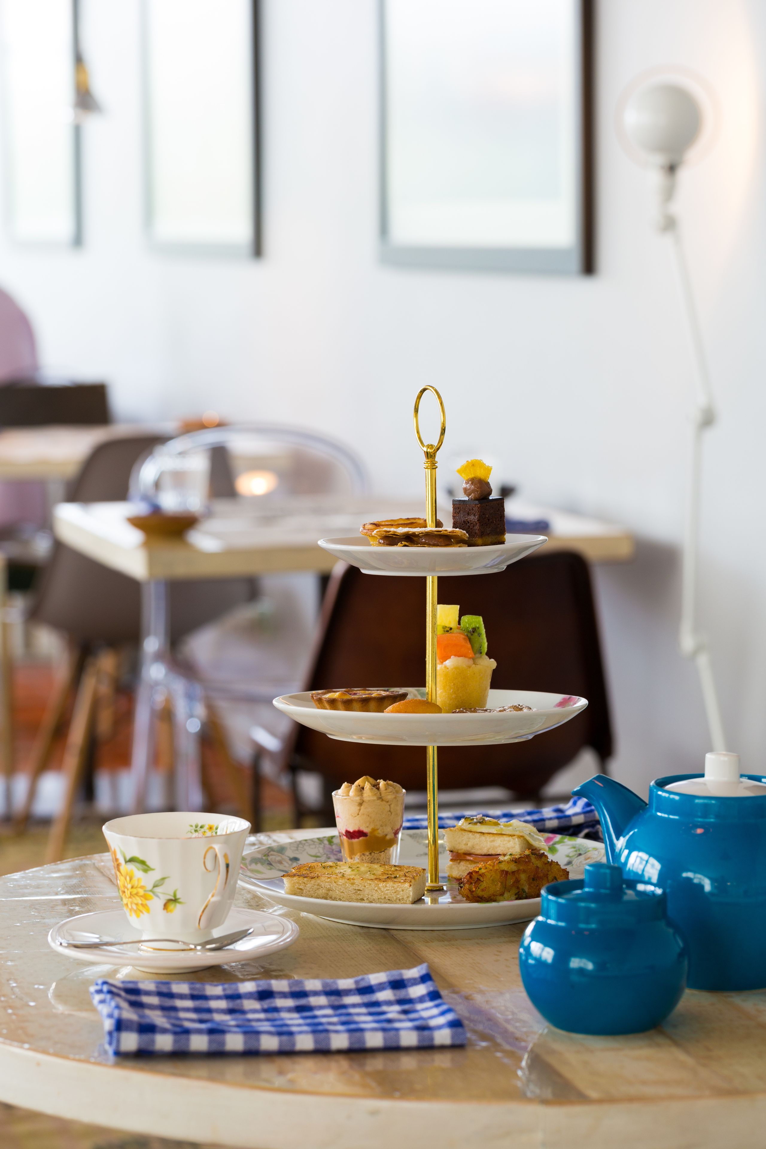 A three-tiered dessert stand with various pastries and a teapot on a table.