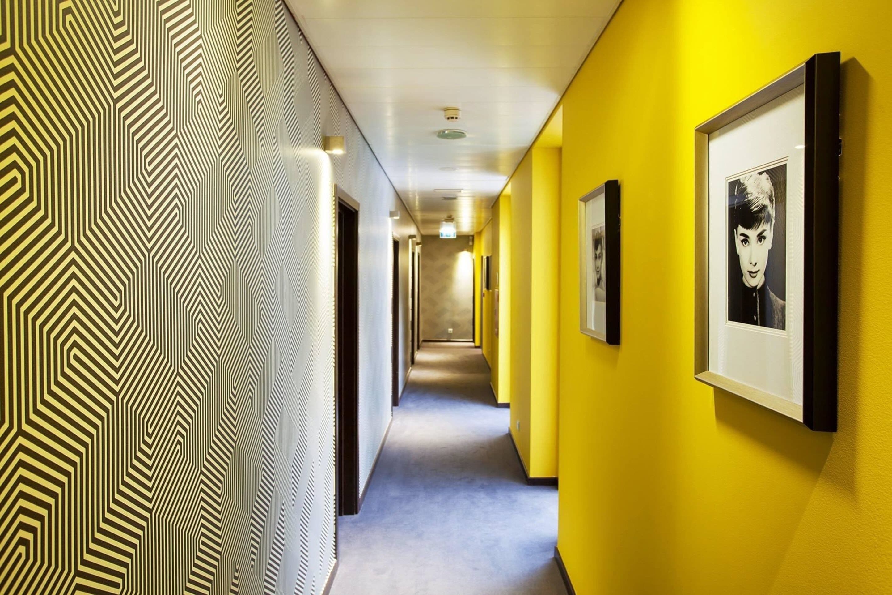 Un couloir avec un papier peint à motifs, des murs jaunes et des œuvres d’art encadrées.
