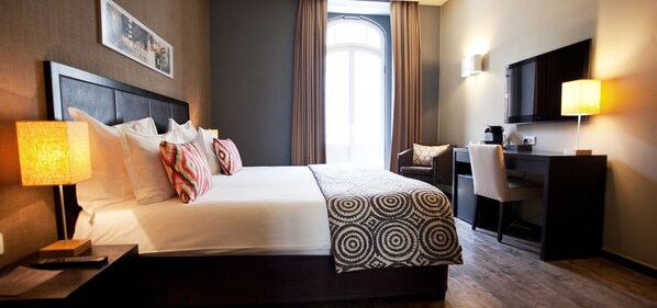 Habitación de hotel con una cama grande, un escritorio, una silla, un televisor y una ventana con cortinas.