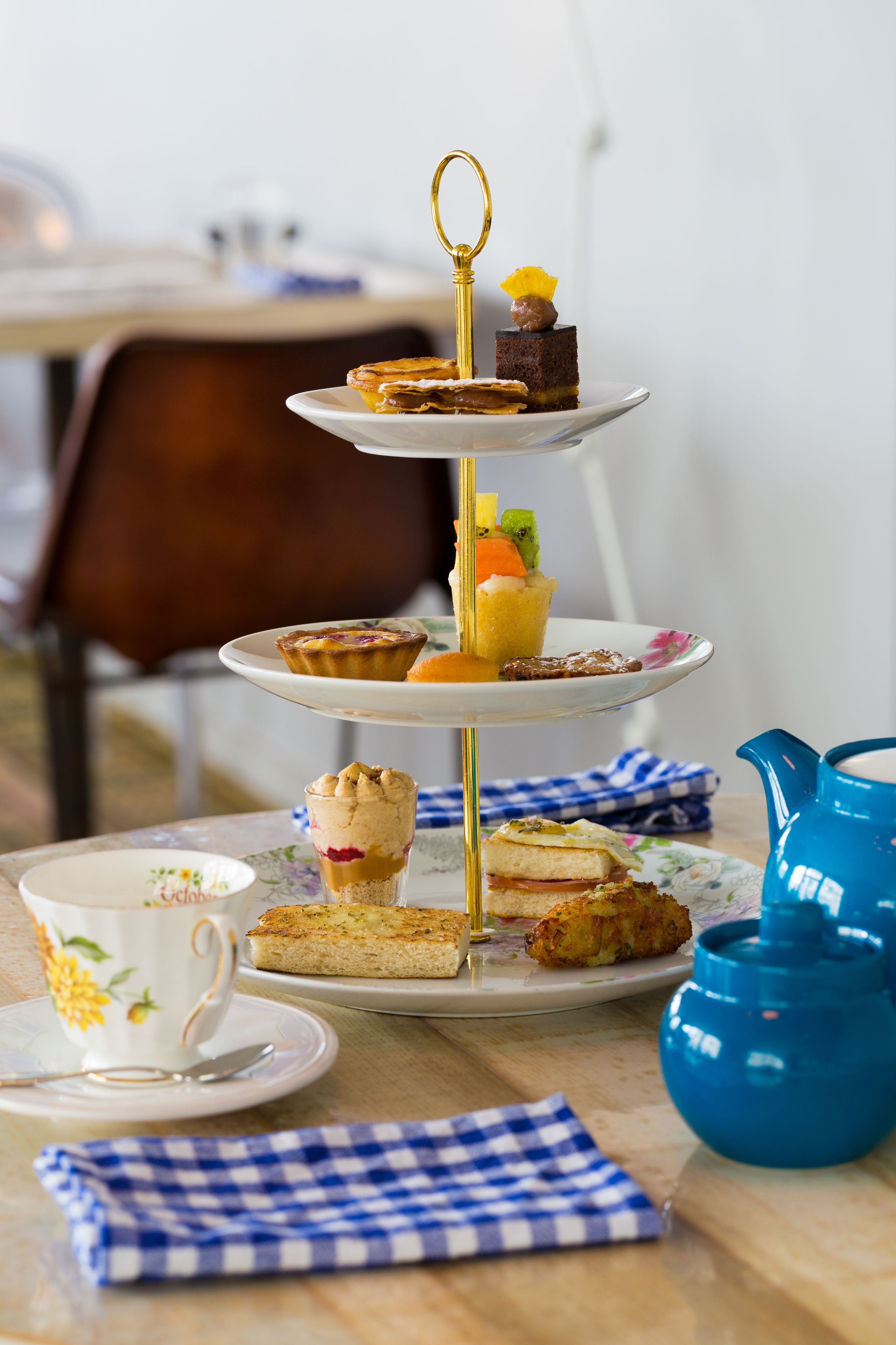 A three-tiered dessert stand with various pastries and a teapot on a table.