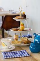 Un présentoir à trois niveaux, garni de diverses pâtisseries, et une théière, le tout posé sur une table.