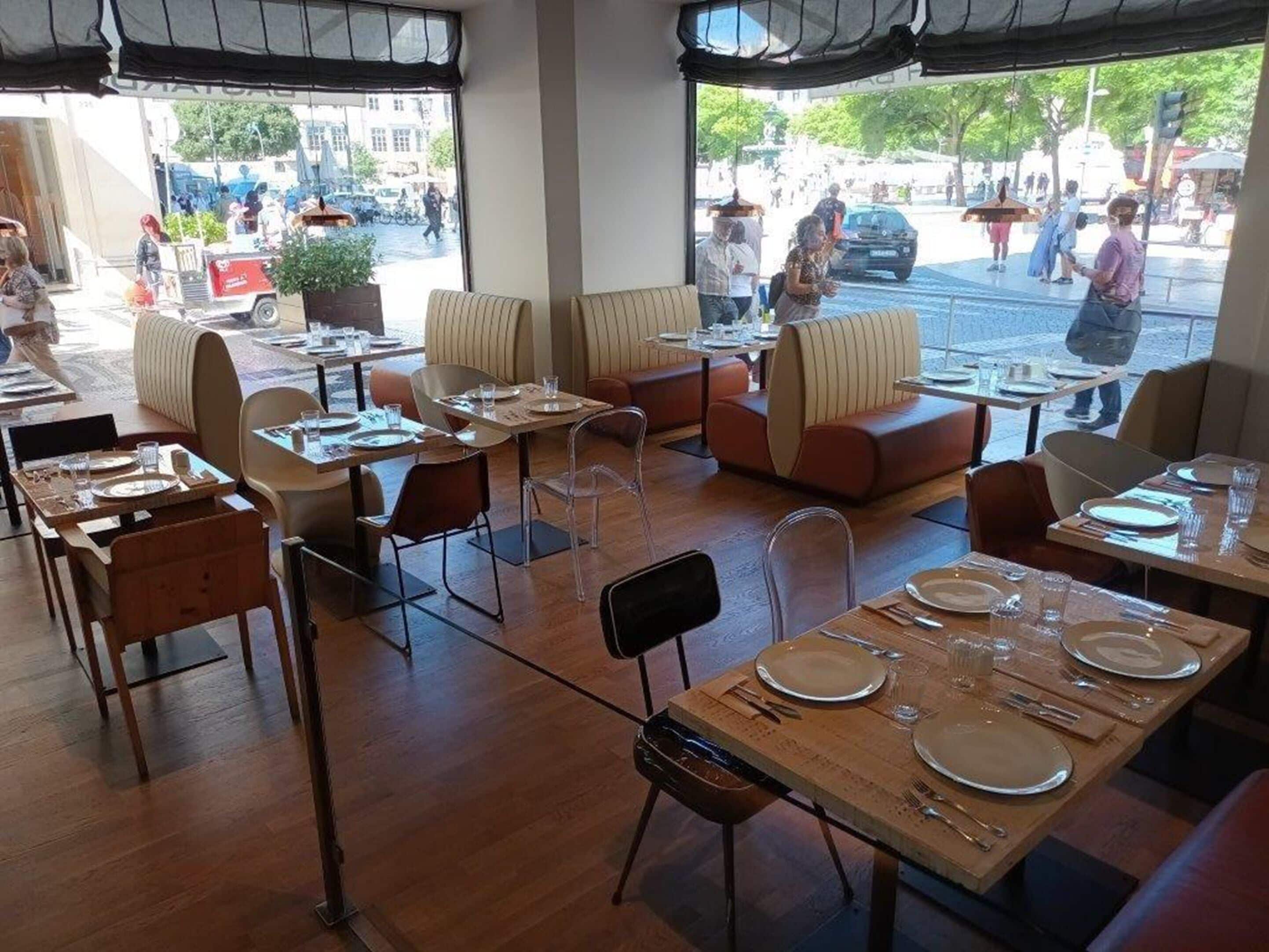Um espaço de refeições interno com mesas e cadeiras, uma grande janela com vista para uma rua movimentada e uma vista da paisagem urbana.