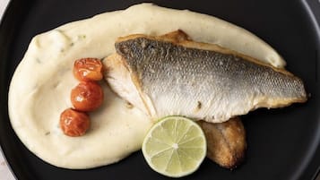 En sort tallerken med fisk, cremet sauce, kirsebærtomater og et stykke lime.