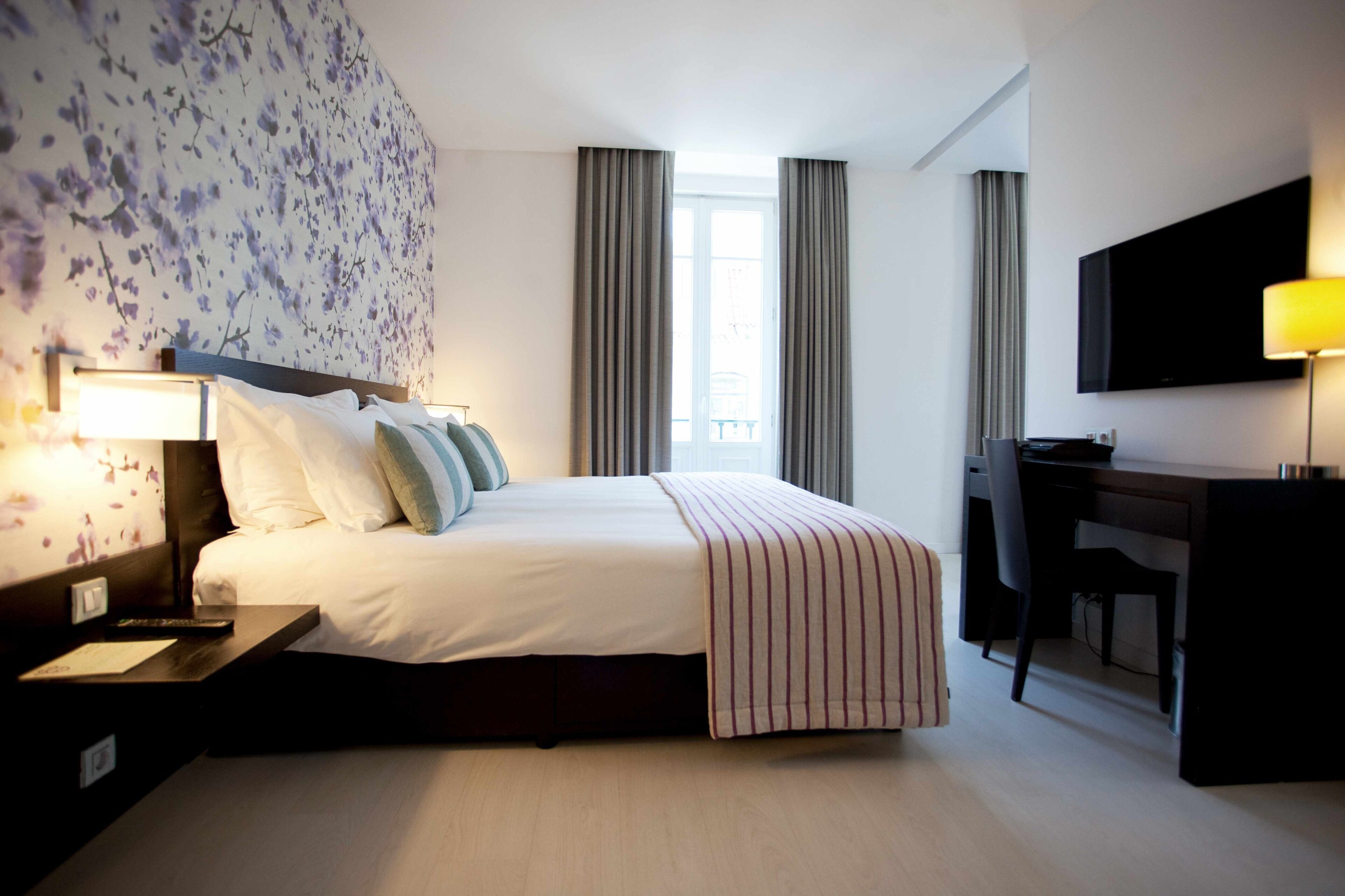 Una camera d'hotel con un letto, una scrivania, una televisione e una finestra con tende.