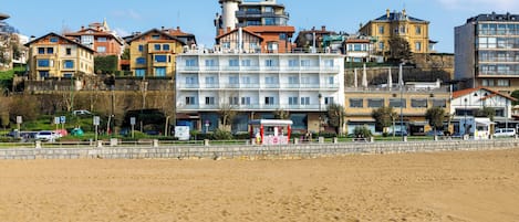 A beachfront hotel with multiple floors, a sandy beach in the foreground, and various buildings in the background.