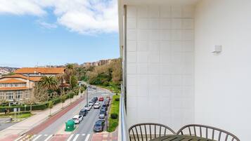 A balcony with a view of a city street, a tiled wall, and a table with chairs.