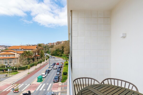 A balcony with a view of a city street, a tiled wall, and a table with chairs.
