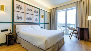 Une chambre d’hôtel avec un grand lit, un bureau, une chaise, un balcon avec vue et des œuvres d’art au mur.