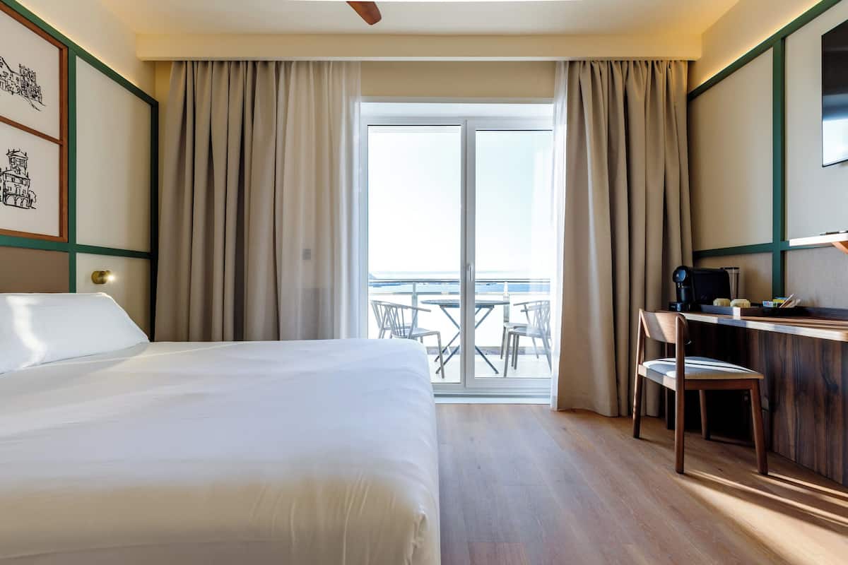 A hotel room with a bed, a desk, and a view of the outdoors.