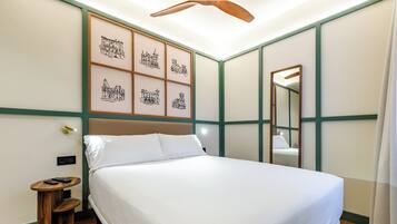 A neatly made bed in a hotel room with a headboard, a small wooden side table with a remote control, and a wall-mounted mirror.
