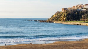 Vista costera con playa, costa rocosa y edificios en una colina.
