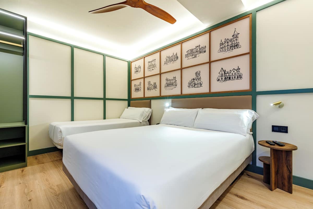 A hotel room with a large bed, two smaller beds, a wooden ceiling fan, and a wall with framed pictures.
