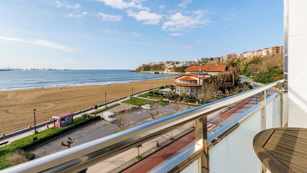 Vista costera desde un balcón con vista a una playa, un estacionamiento y un edificio con techo rojo.